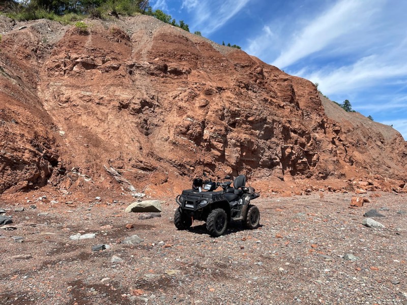 An ATV parked on the beach below the red cliffs of the Parrsboro shore