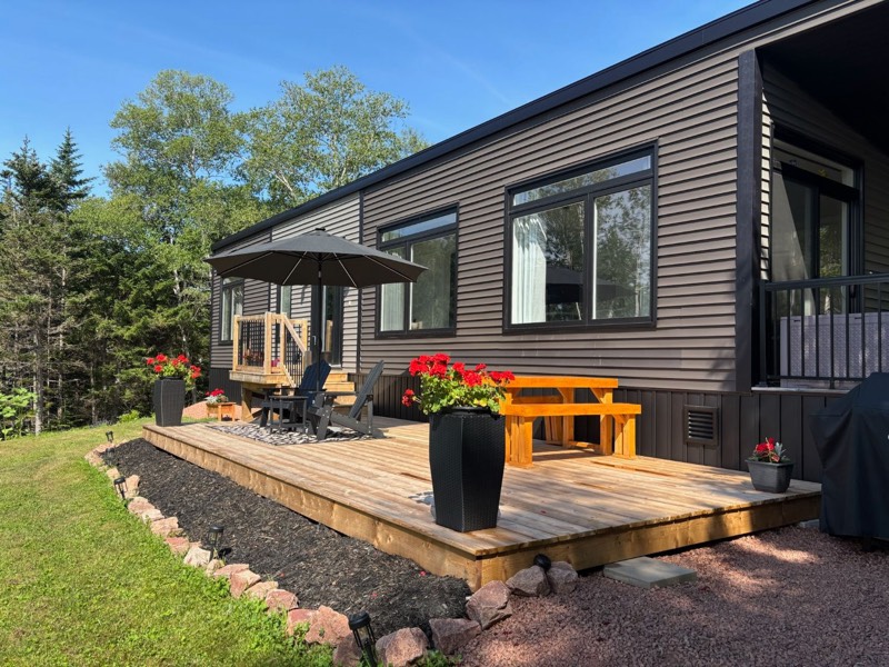 The sunny deck at Tides and Trails Cottage with a patio umbrella, Adirondack chairs, picnic table and red geraniums