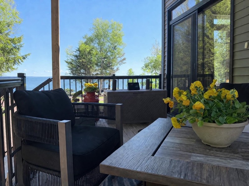 Covered deck with cushioned outdoor seating and potted flowers looking out to the Bay of Fundy