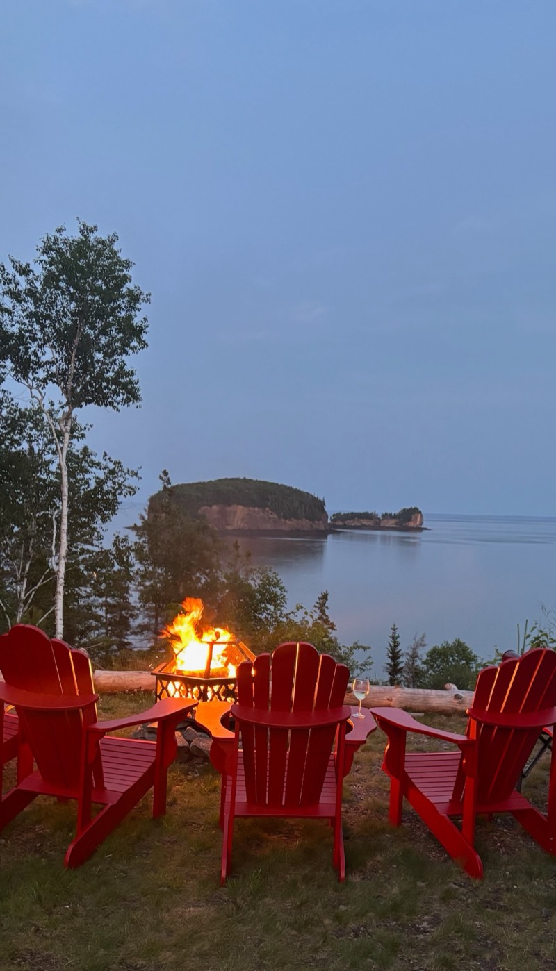 Red Adirondack chairs around a fire at dusk, facing the Two Islands