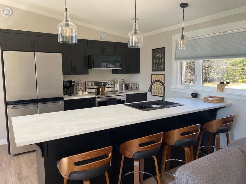 Fully equipped kitchen with black cabinets, a large island and four bar stools
