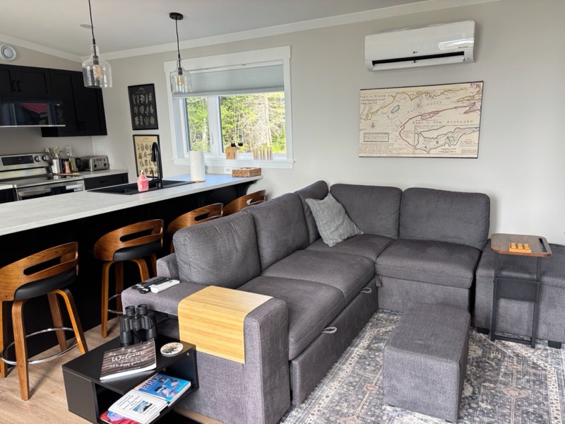 Open-plan living room with a grey sectional, kitchen island and a vintage Bay of Fundy map