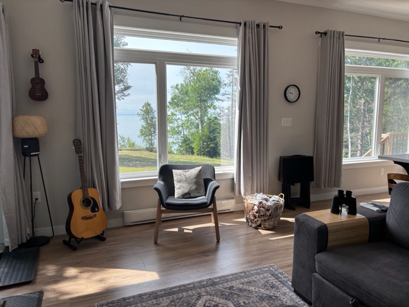 Bright living room with a guitar, armchair and large windows looking out to the Bay of Fundy