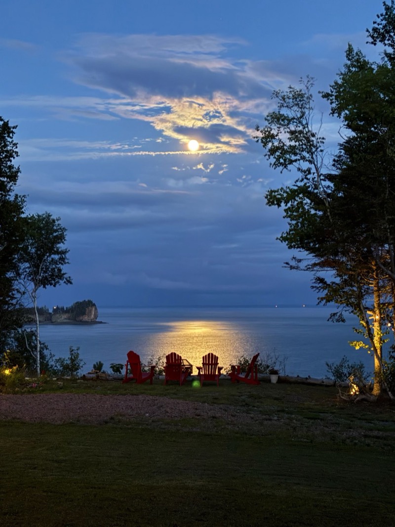 Full moon rising over the Bay of Fundy behind four red Adirondack chairs